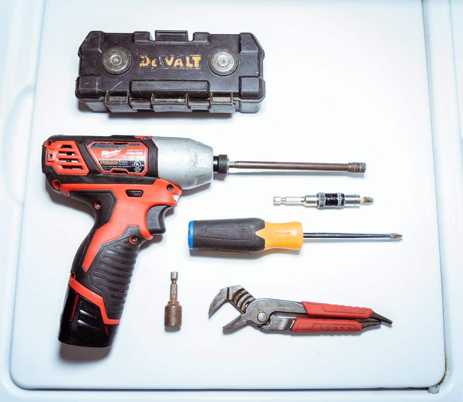 Impact driver, screwdrivers, and pliers a Doctor Maintenance technician uses on a Baltimore, MD appliance repair, laid out on a washer