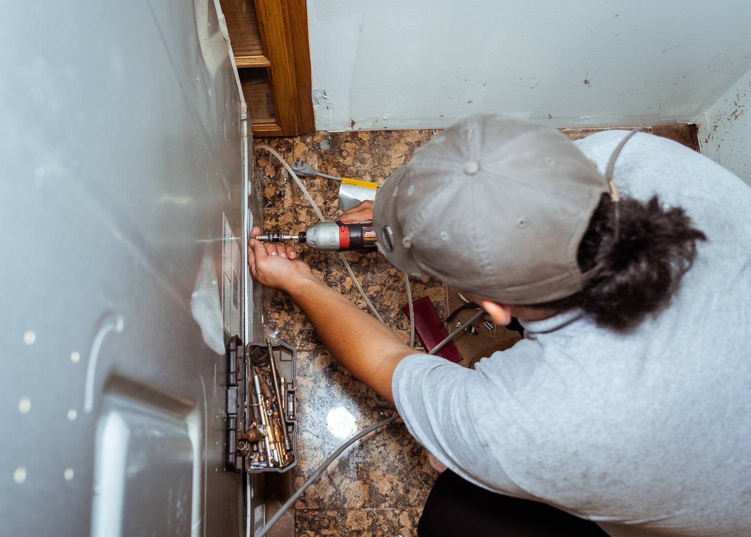 Doctor Maintenance technician removing a refrigerator’s rear access panel in Baltimore, MD to inspect the condenser fan, condenser coils, and compressor