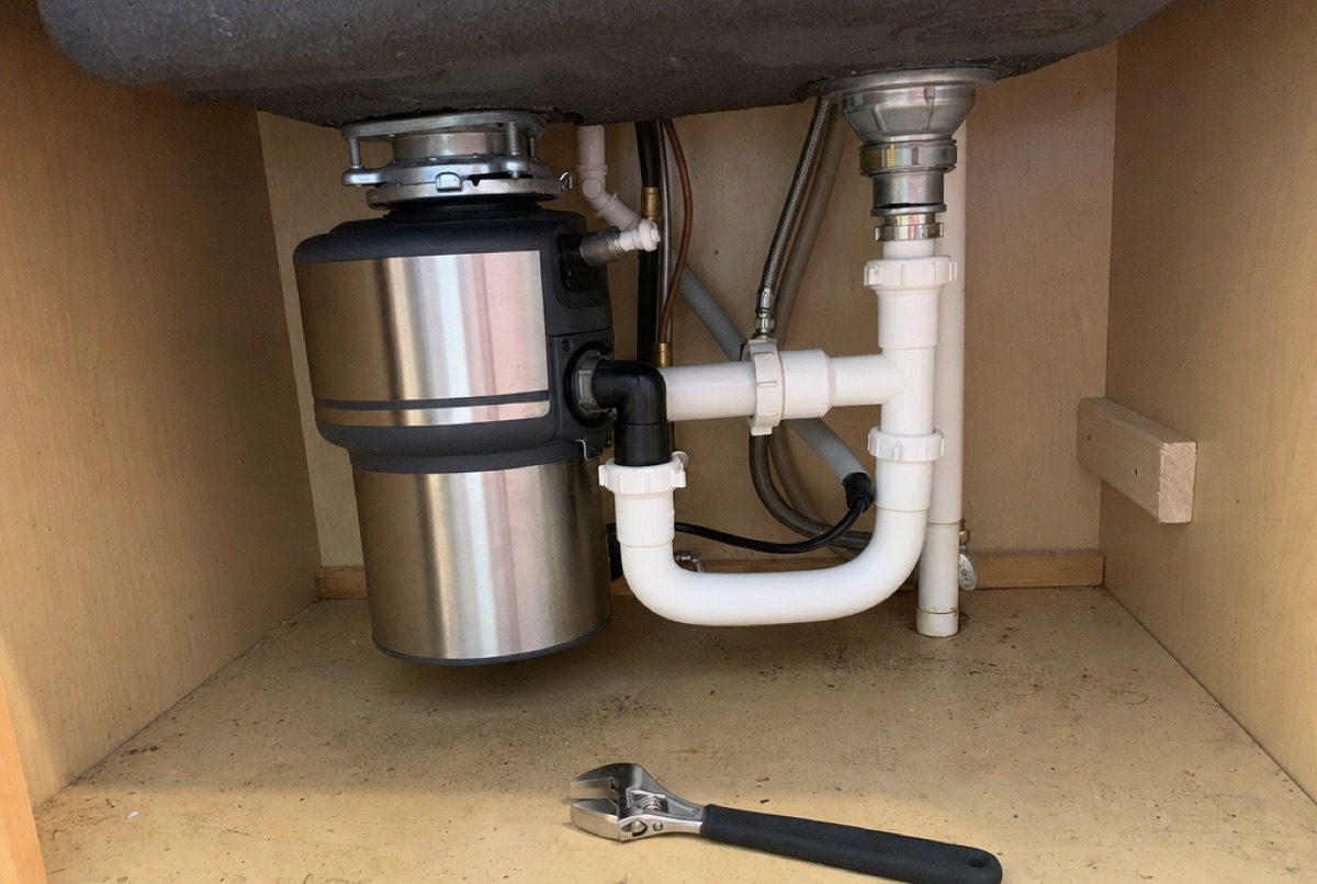 Bottom of the unit view of a garbage disposal under a Baltimore, MD kitchen sink, where Doctor Maintenance techs insert the hex wrench and press the red reset button to free a stuck flywheel and remove debris